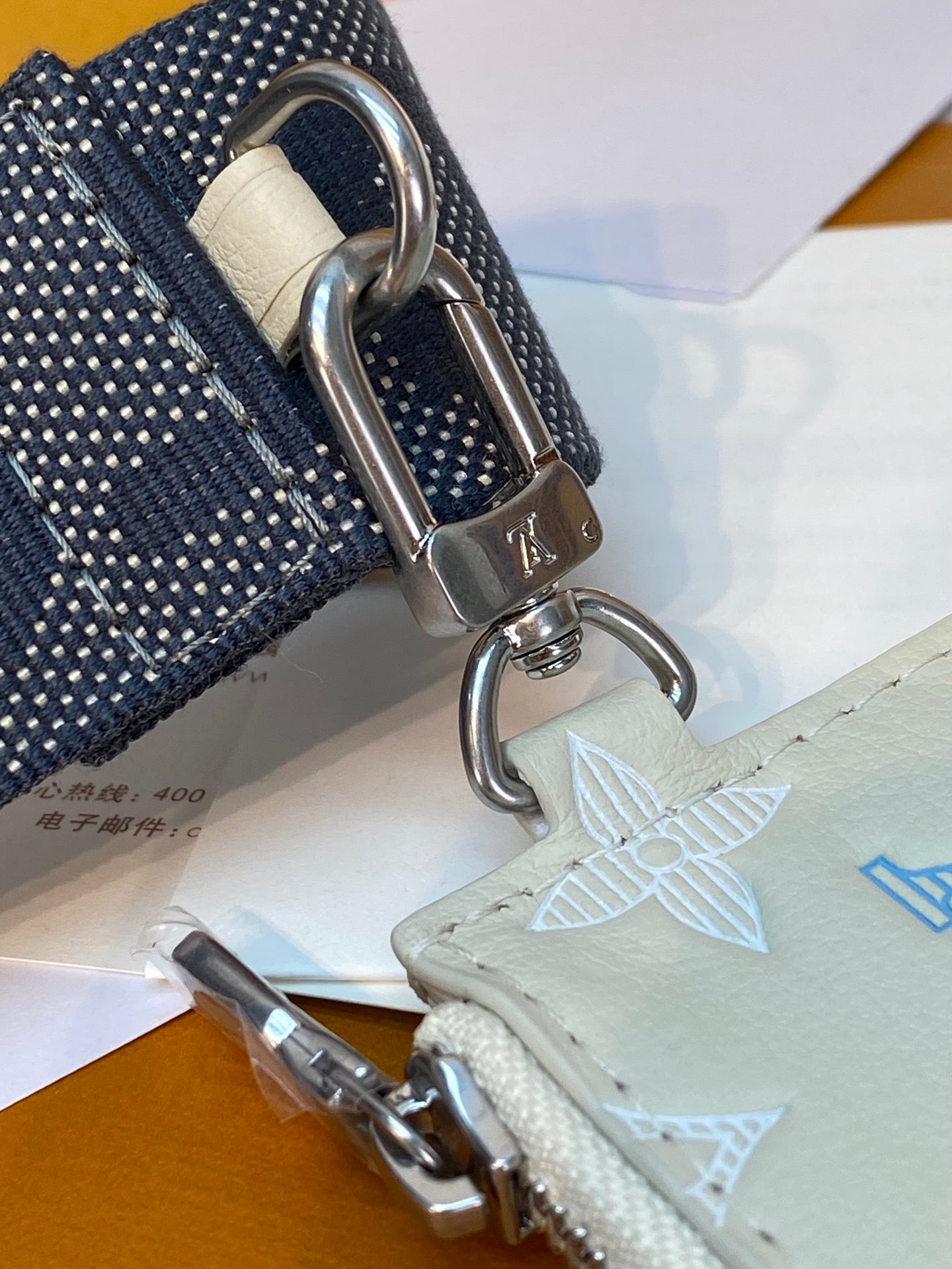 Navy strap with silver clasps attached to cream monogram pouch