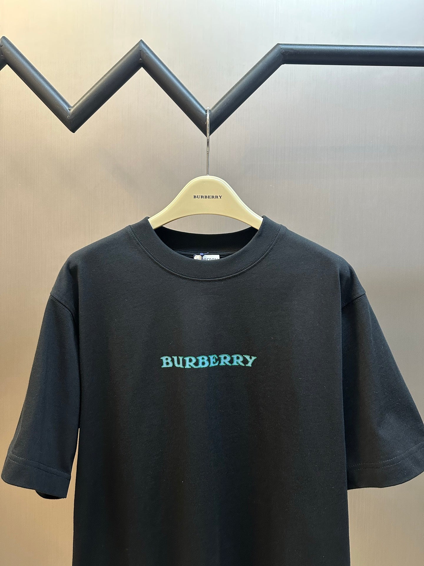 Black short-sleeve T-shirt with Burberry logo text in teal on front