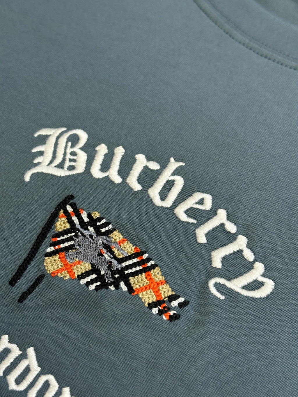 Close-up of embroidered Burberry logo graphic on blue short-sleeve T-shirt