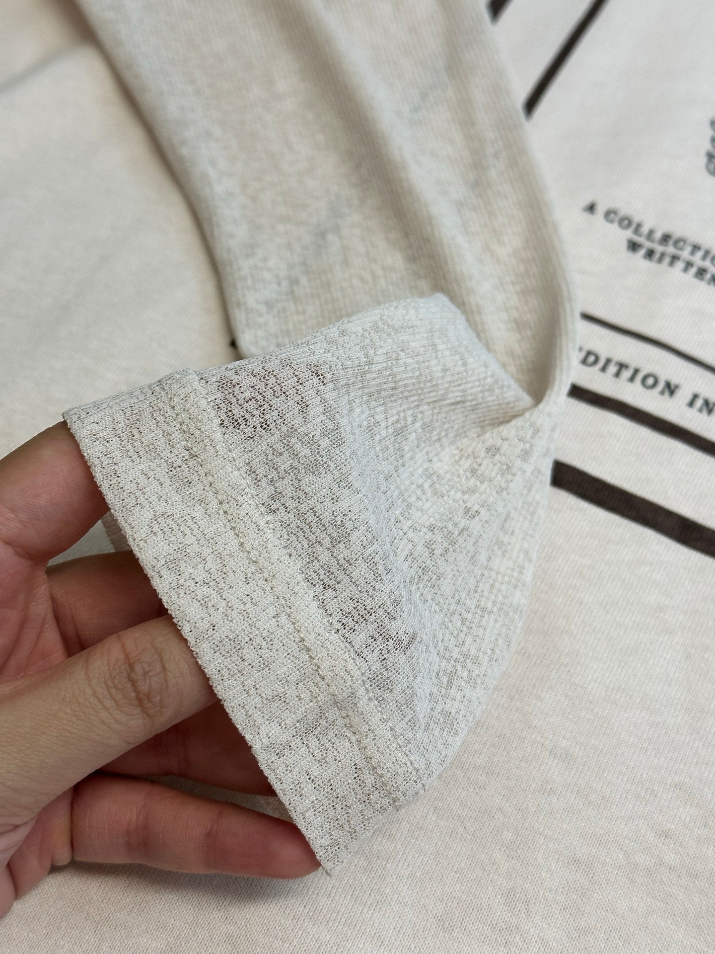 Cream T-shirt cuff and hem with texture detail, held in hand