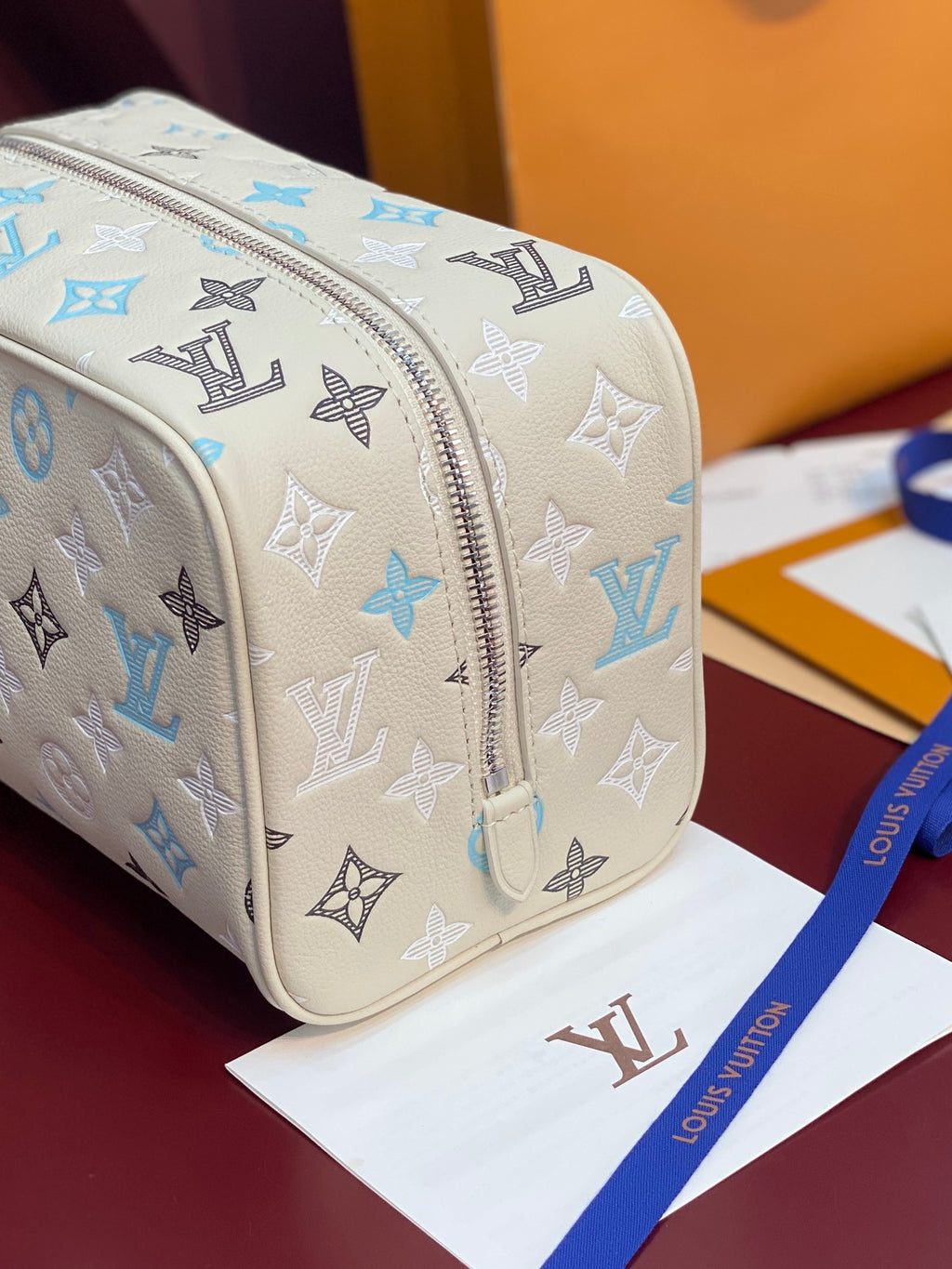 Louis Vuitton toiletry bag close-up: blue and black monogram on light beige with metal zipper