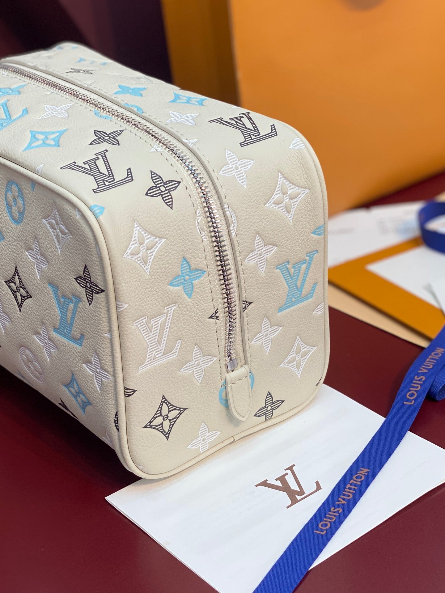 Louis Vuitton toiletry bag close-up: blue and black monogram on light beige with metal zipper