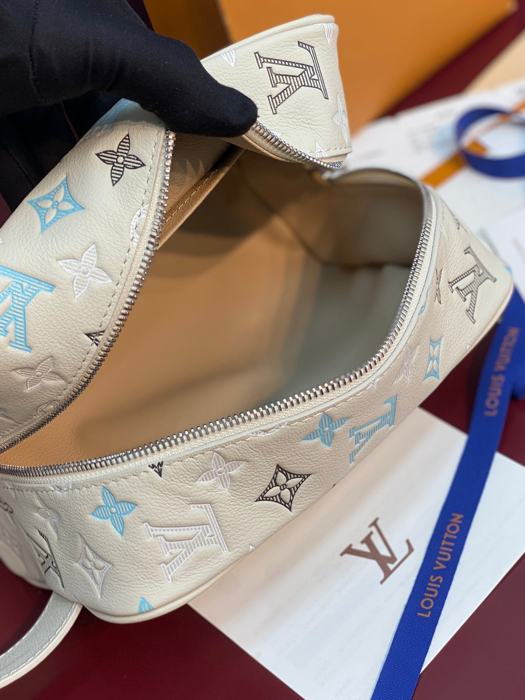 Louis Vuitton toiletry bag open, showing light beige interior and blue-and-black monogram canvas