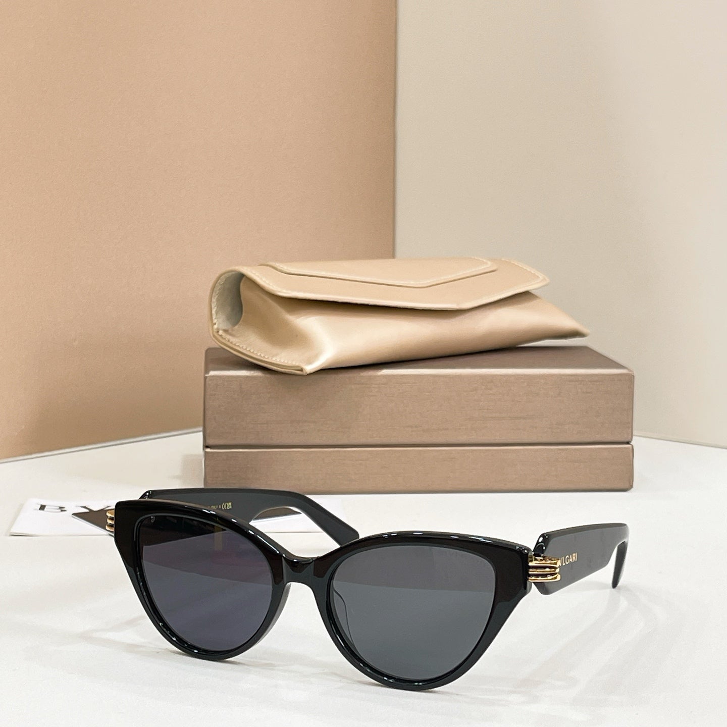 Black cat-eye glasses with dark lenses and gold-tone hinge logo on the temples