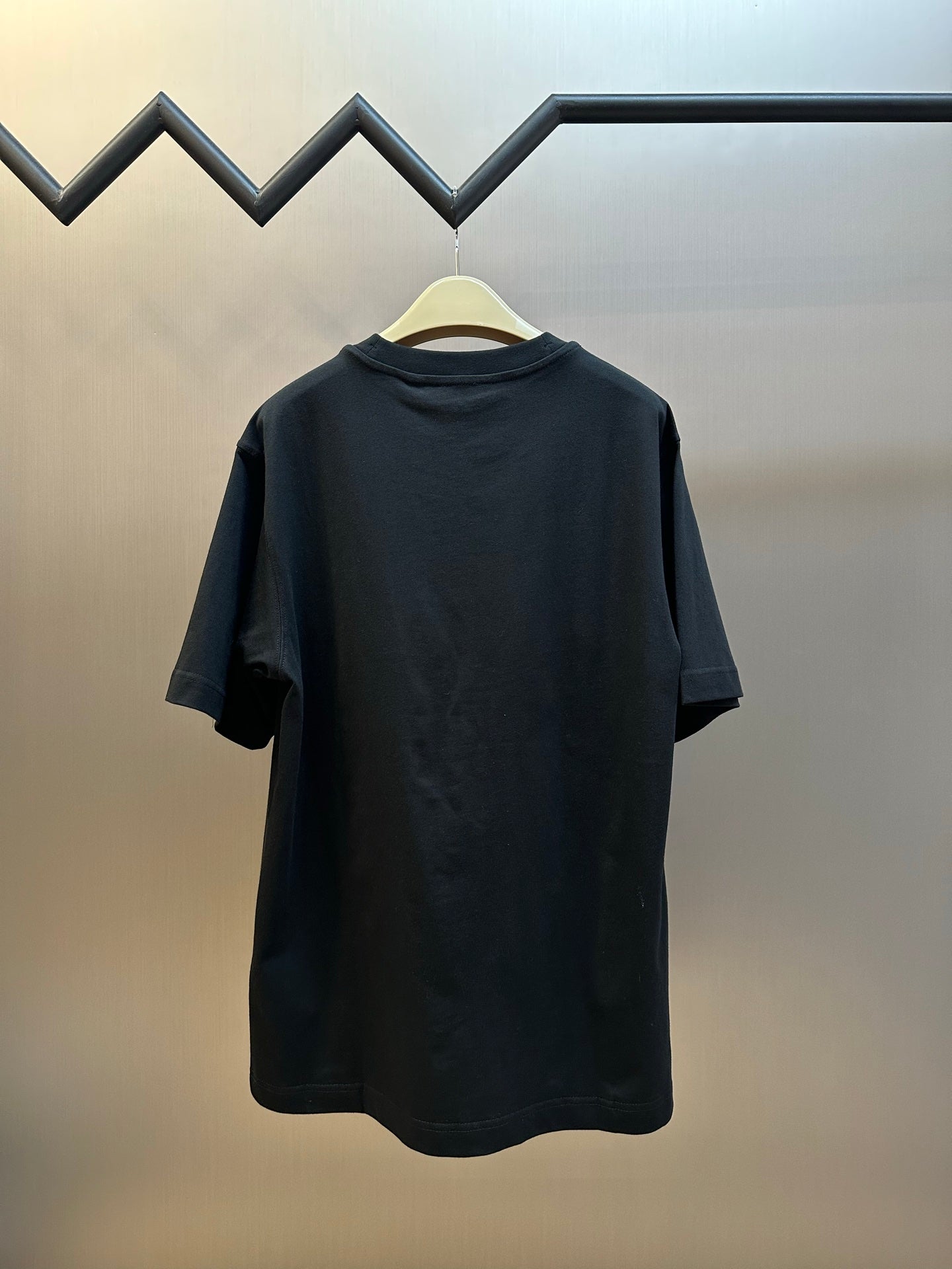 Black short-sleeve T-shirt back view on a hanger, plain design.