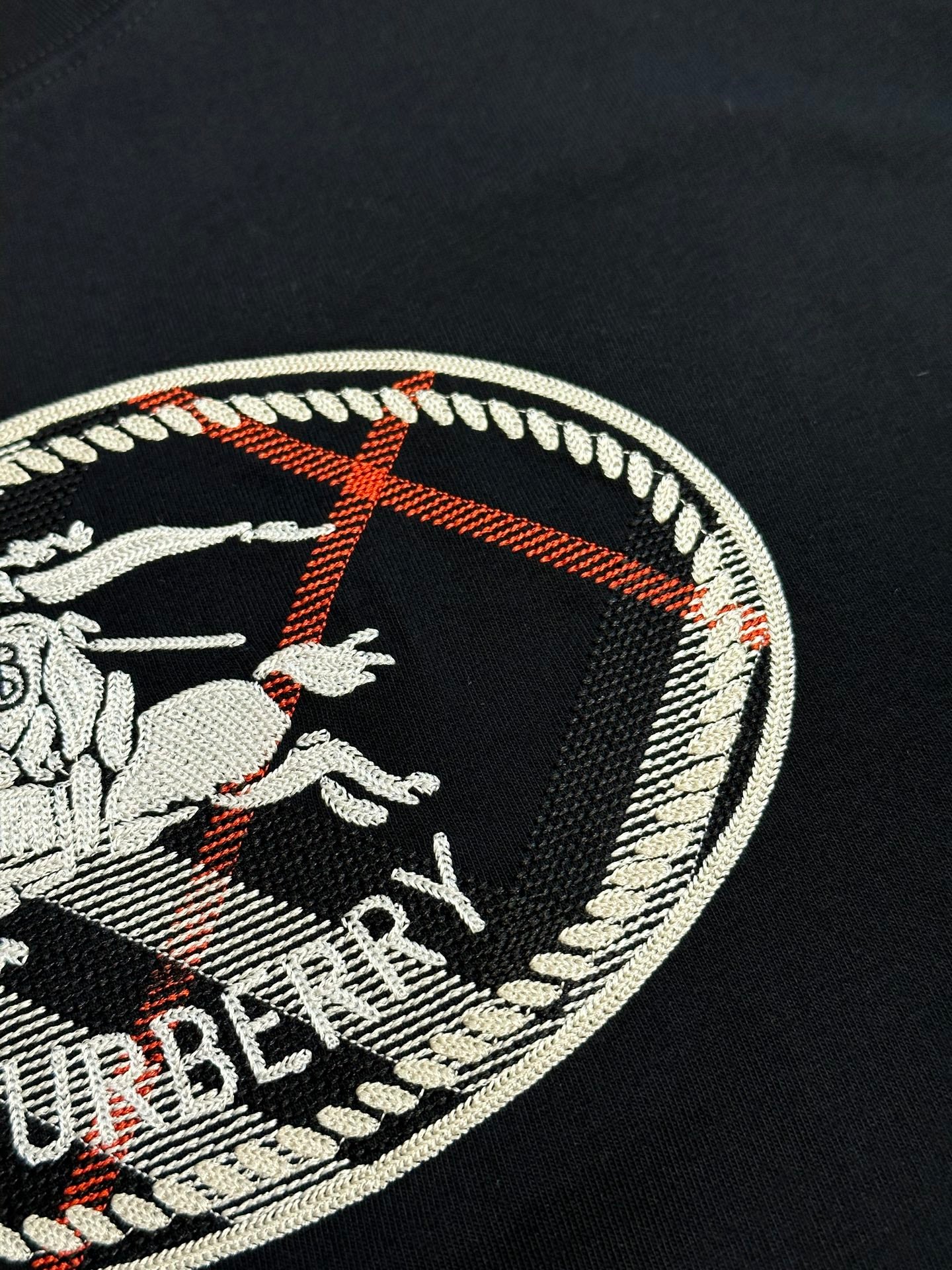 Close-up of oval Burberry logo embroidery on a black T-shirt chest.