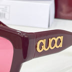 Gucci glasses close-up: burgundy frames with large gold 'gucci' logo on temple.