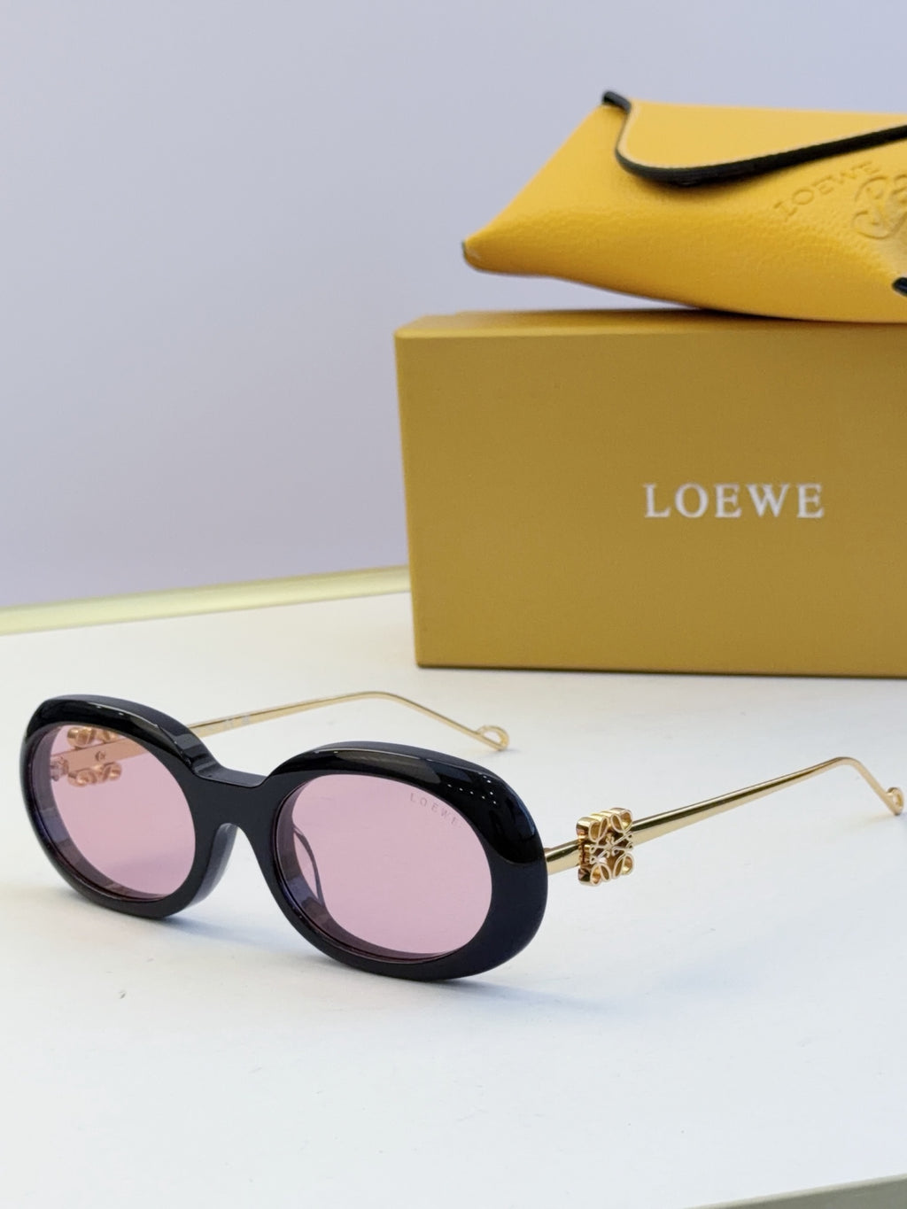 Black round sunglasses with gold-tone hinges and pink-purple tinted lenses