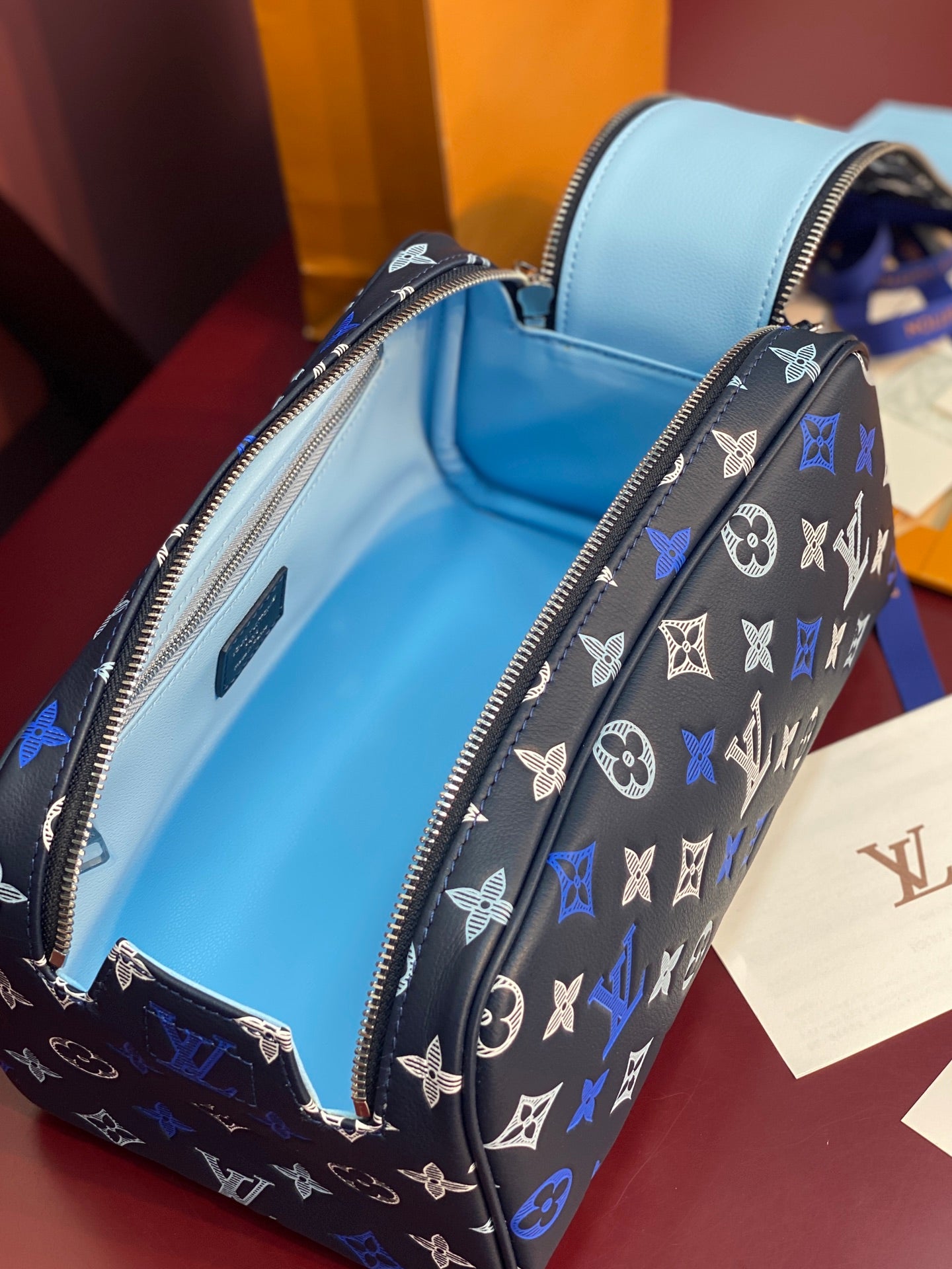 Louis Vuitton bag interior view, light blue lining with embossed label and zipper.