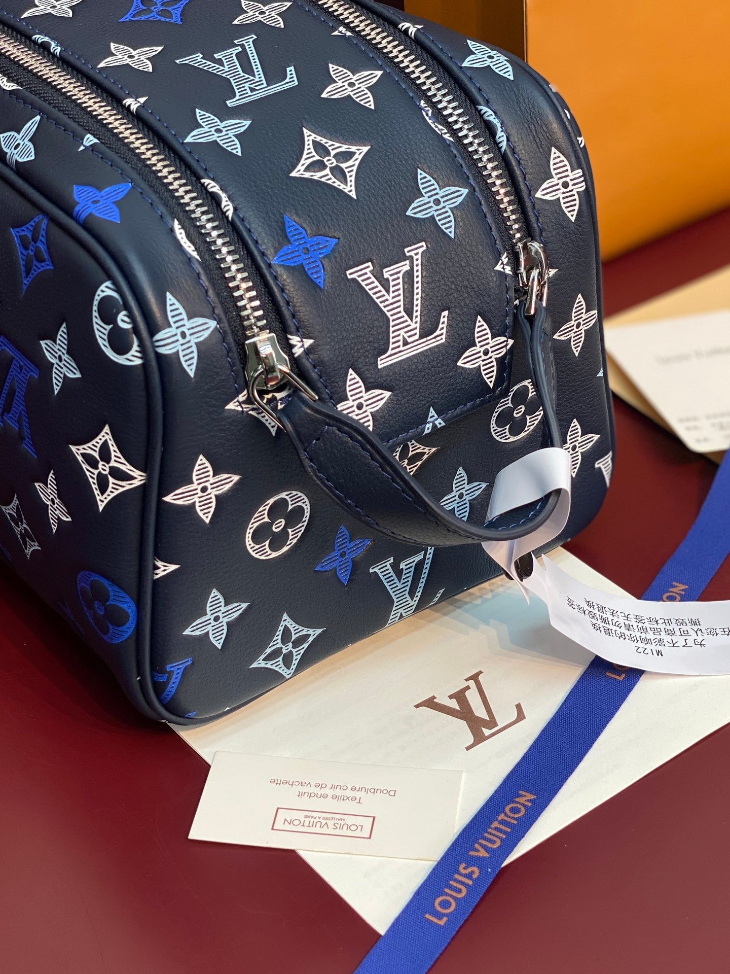 Louis Vuitton bag side view, black fabric with blue monogram, adjustable strap and hang tag.