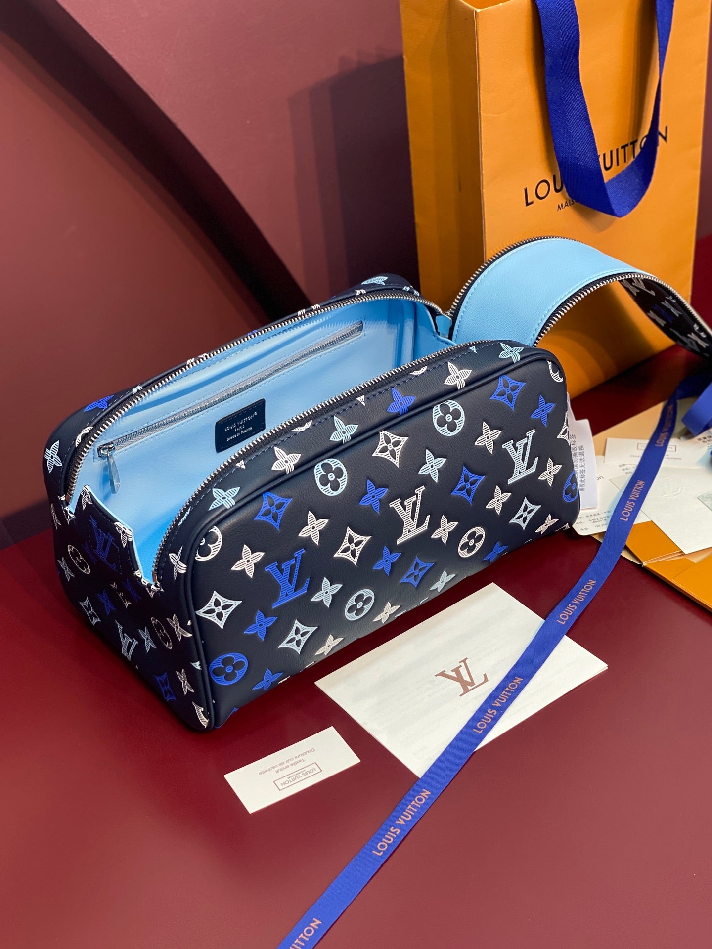 Louis Vuitton bag with black-blue monogram and light blue interior, open top zip.