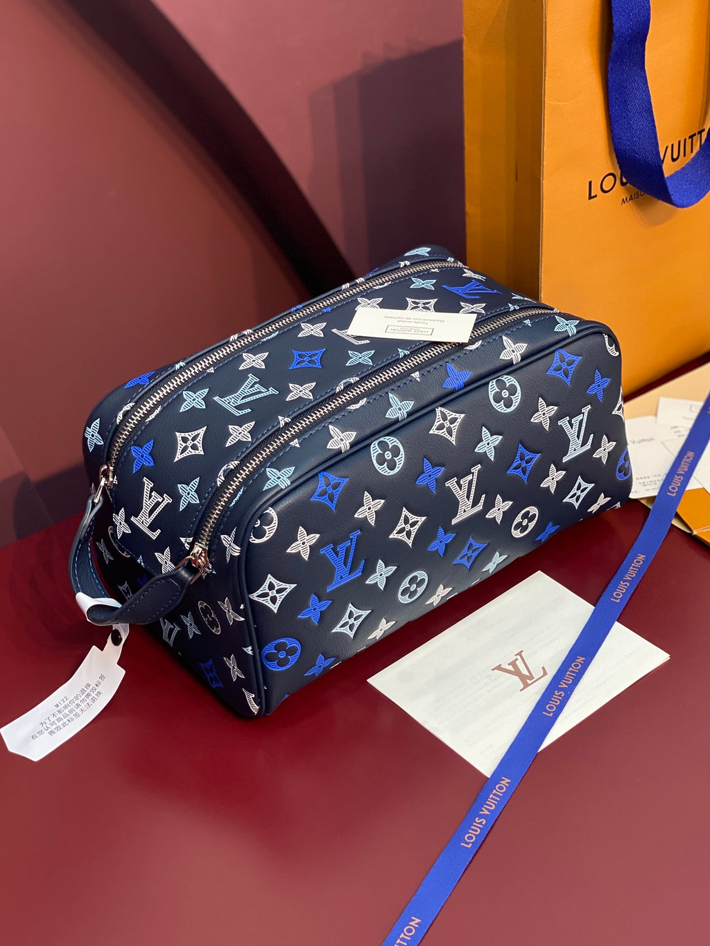 Louis Vuitton bag with black-and-blue monogram, top zipper, navy strap, pebbled finish.