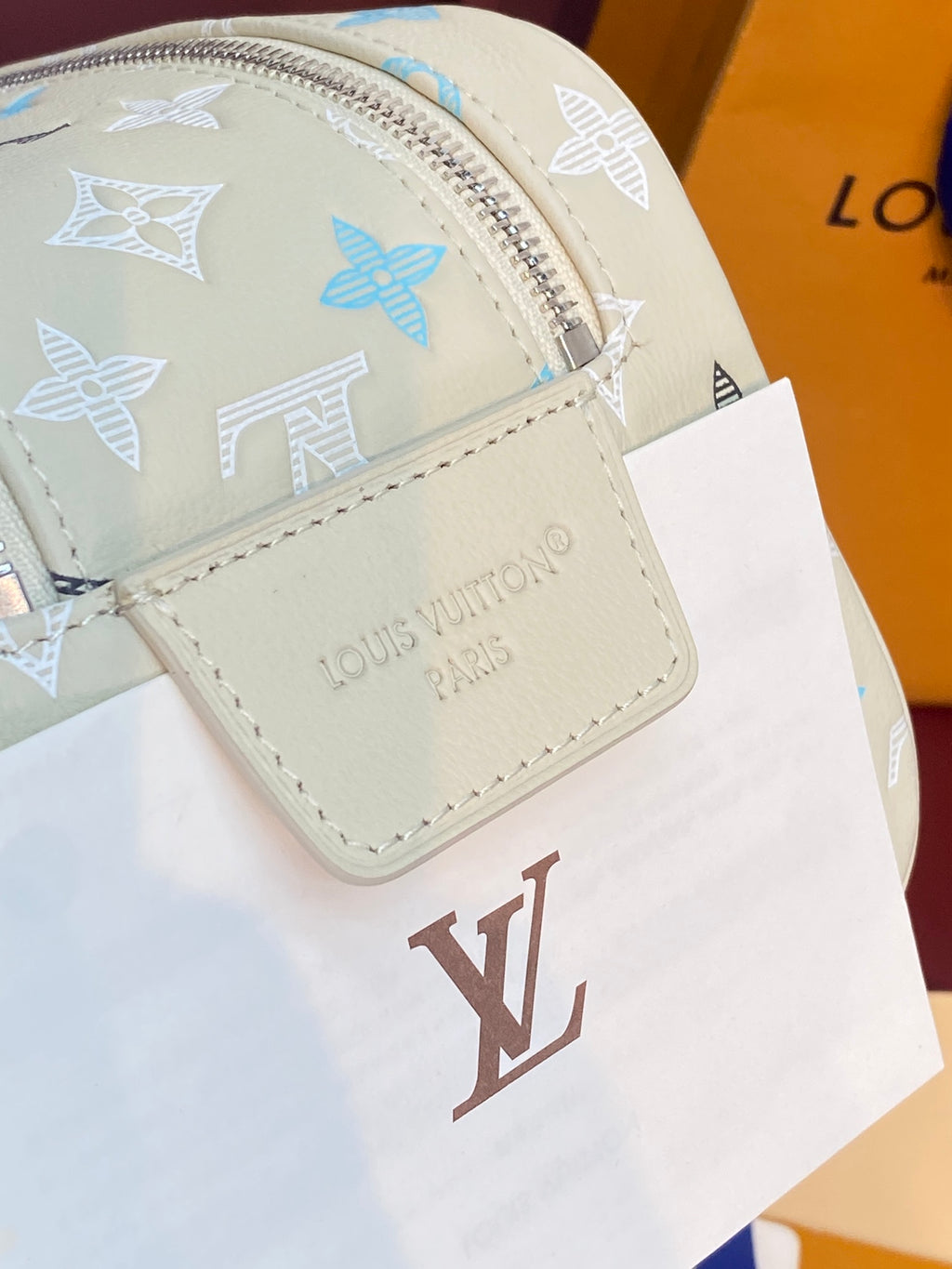 Louis Vuitton monogram bag close-up with light beige patch, blue motifs, and LV emblem