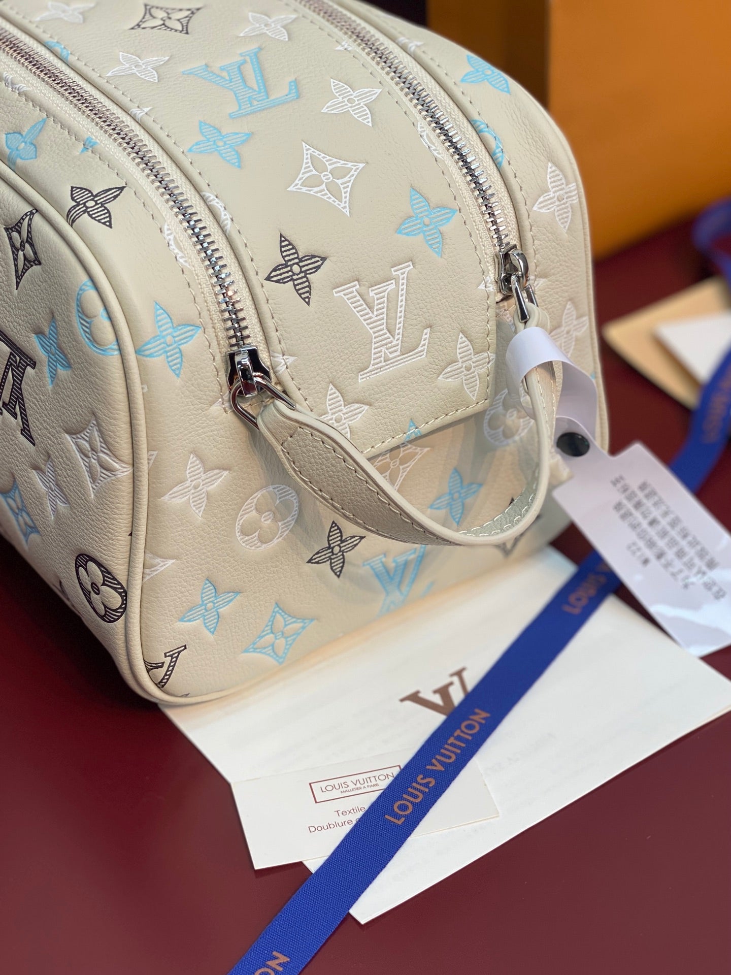 Louis Vuitton monogram bag with light beige strap, blue motifs, and silver zipper pull