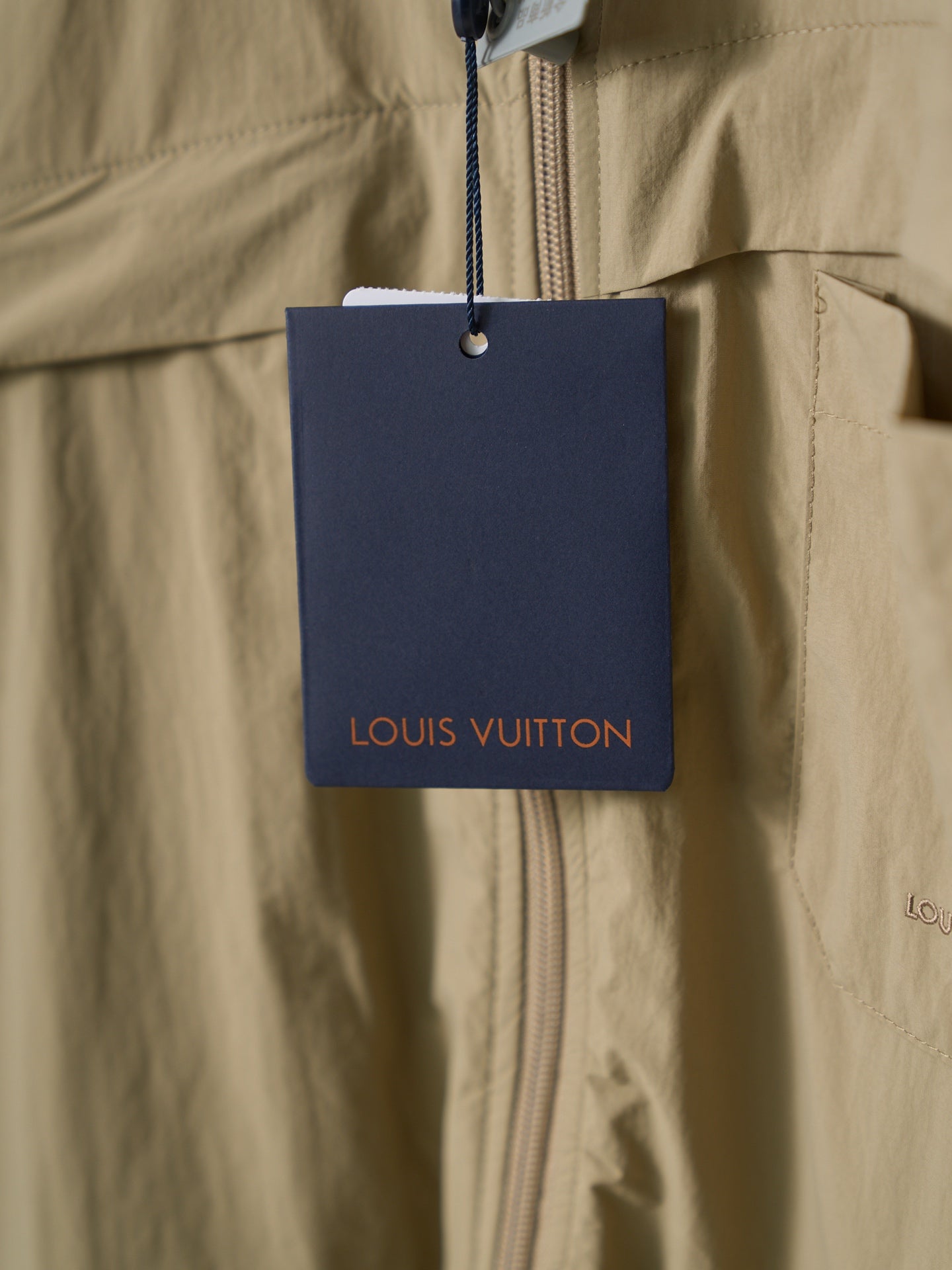 Louis Vuitton price tag hanging from light tan shirt zip front