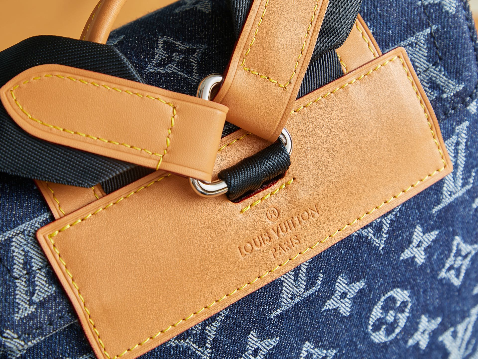 Close-up of tan leather strap ends and metal rings on blue monogram duffel