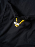 Fendi dark jacket fabric close-up with yellow logo patch and white hang tag
