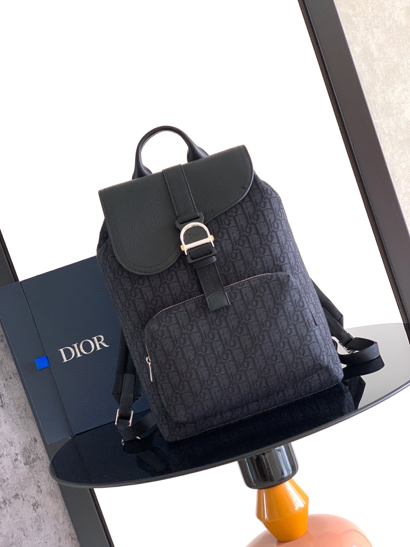 Navy Dior backpack with front flap, metal buckle, and top handle loop