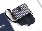 Dior crossbody bag laid flat, navy-beige logo canvas with black leather base