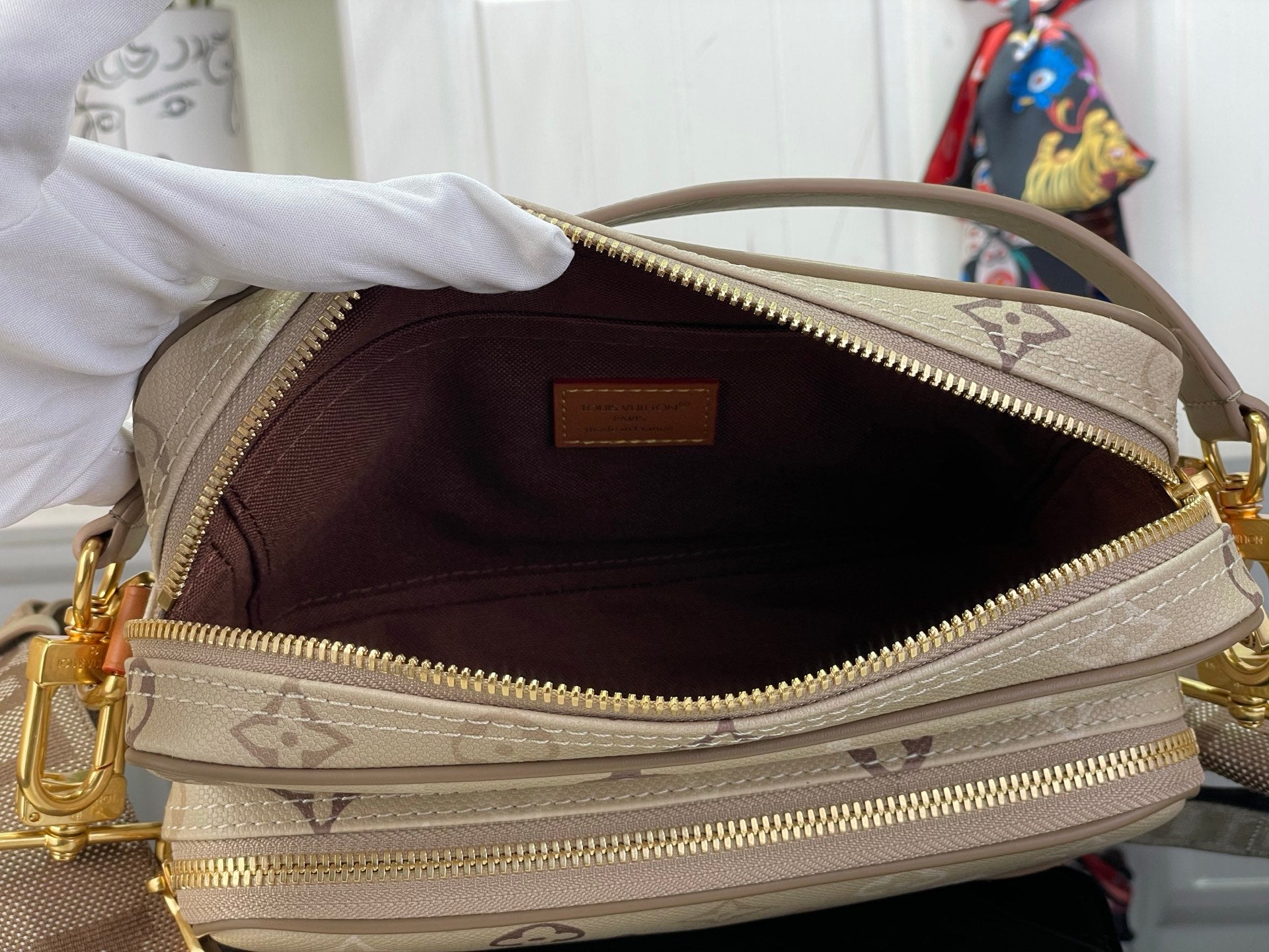 Open beige monogram bag showing dark interior and gold zipper, with logo lining.