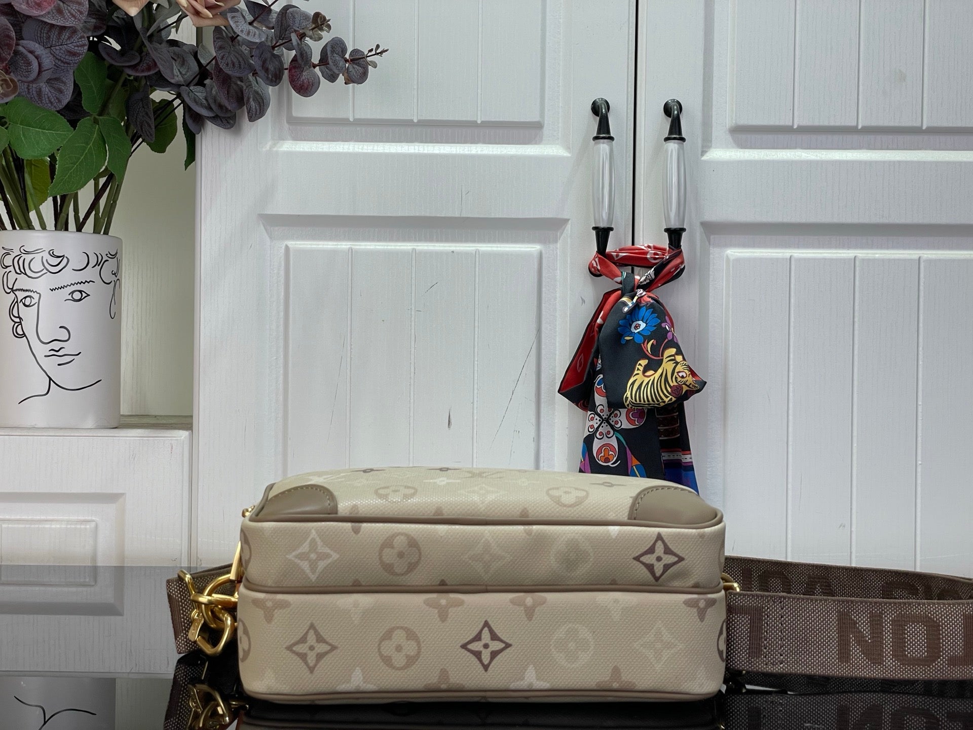 Beige monogram crossbody bag with front panel and gold-tone clasp, short handle.