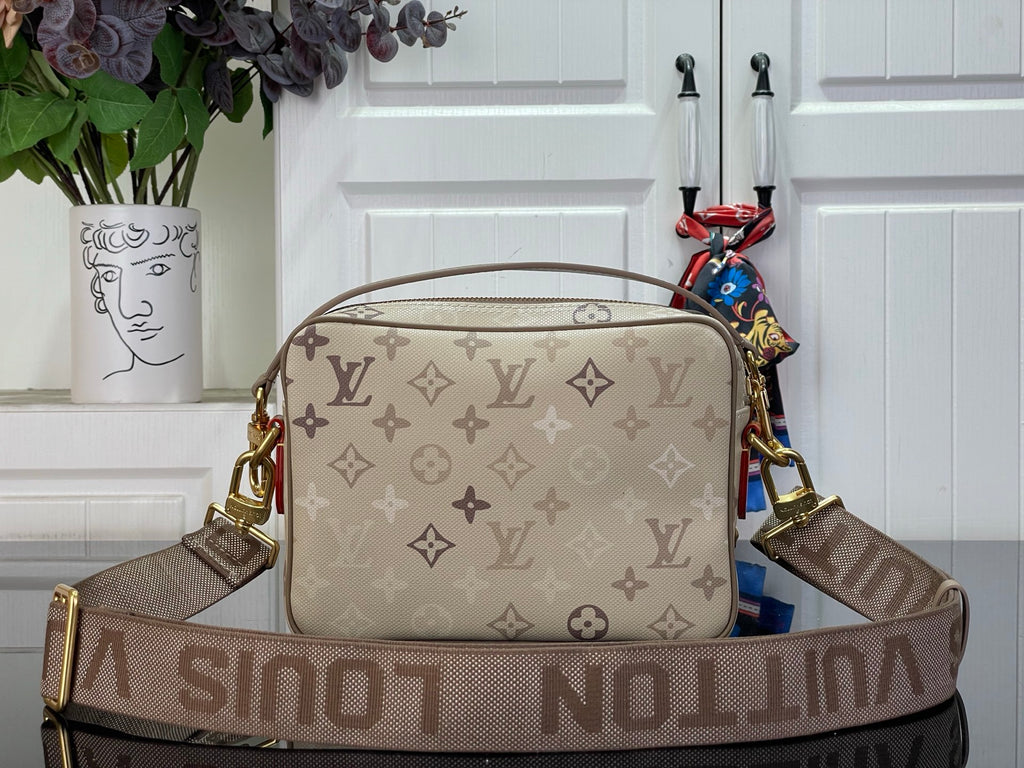 Beige monogram crossbody bag with wide patterned strap and gold-tone hardware.