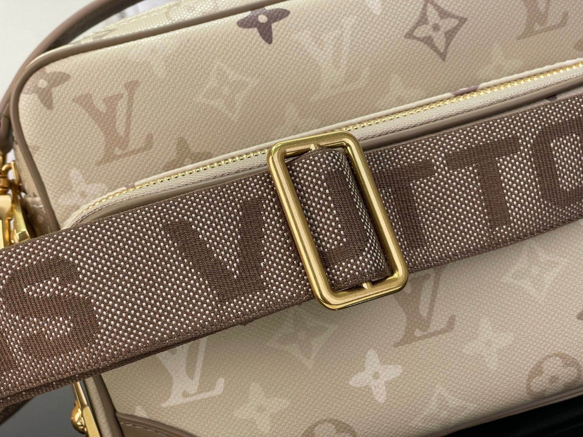 Beige monogram shoulder strap with gold buckle and repeated logo pattern.