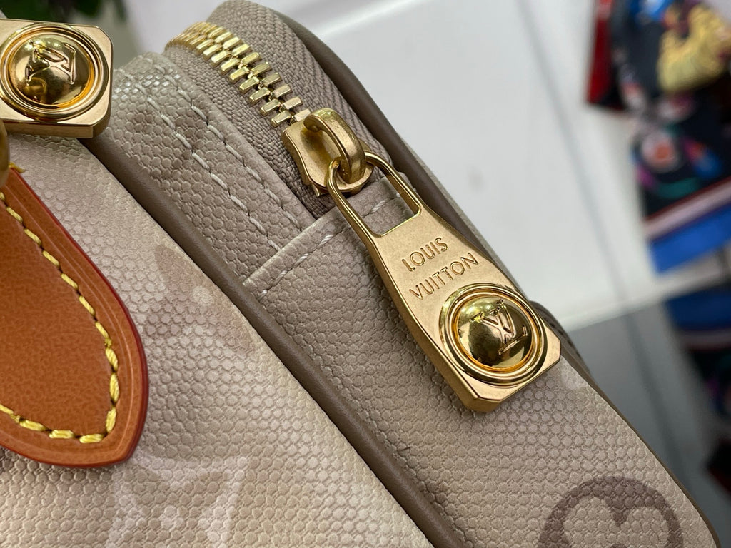 Beige textured monogram bag corner with gold-tone ring clasp and stitched trim.