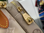 Beige textured monogram bag corner with gold-tone ring clasp and stitched trim.