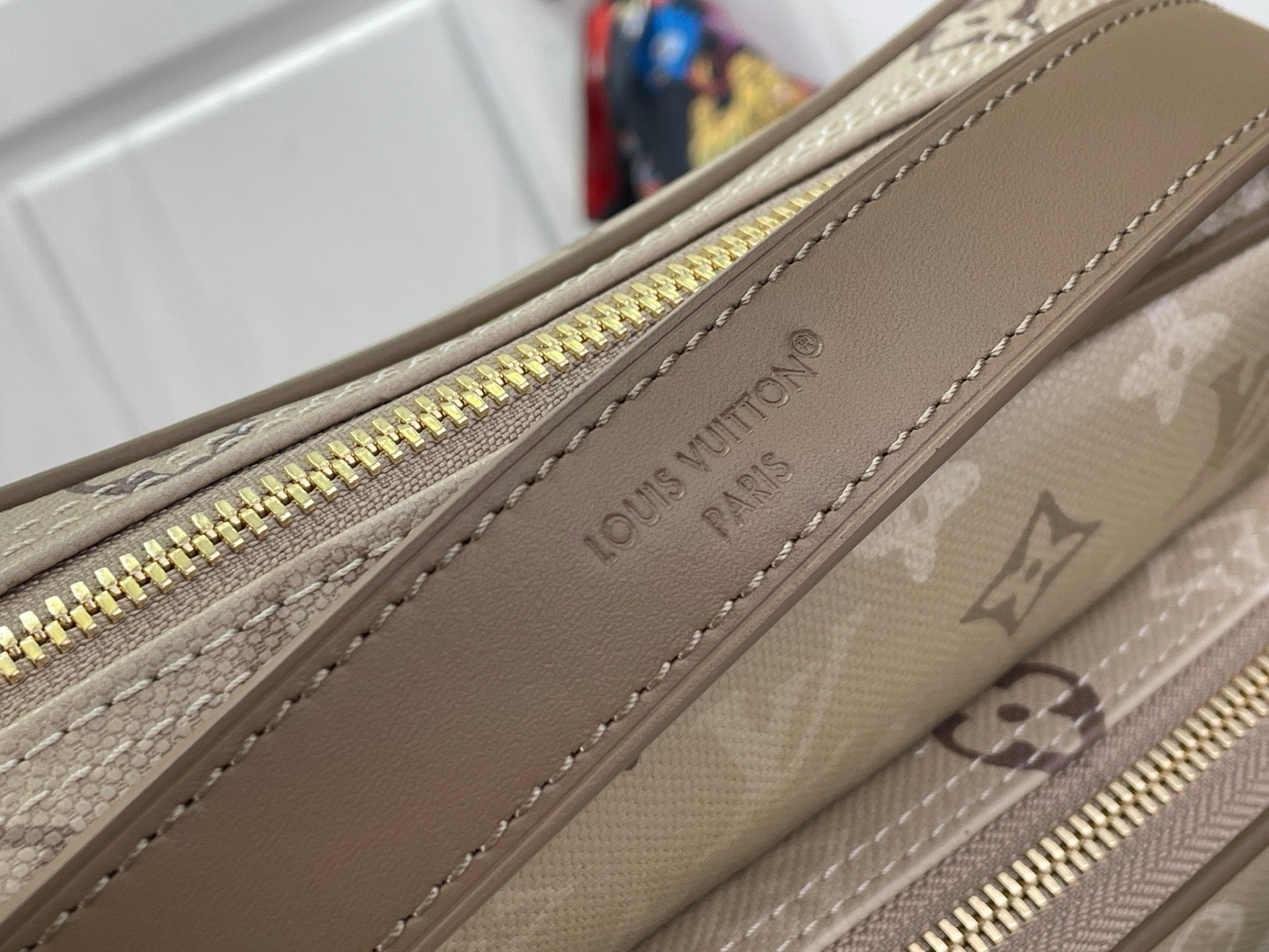 Beige monogram bag with zipper track and brown leather edge trim, gold zipper pull.