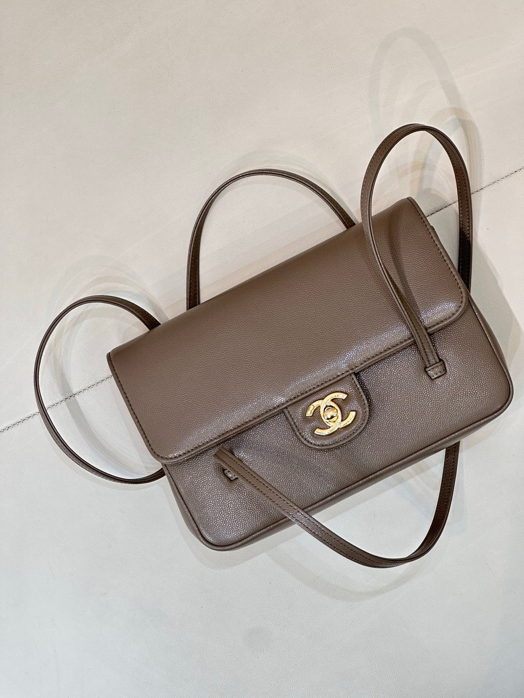 Taupe Chanel shoulder bag angled view with top handle, flap, and gold CC emblem