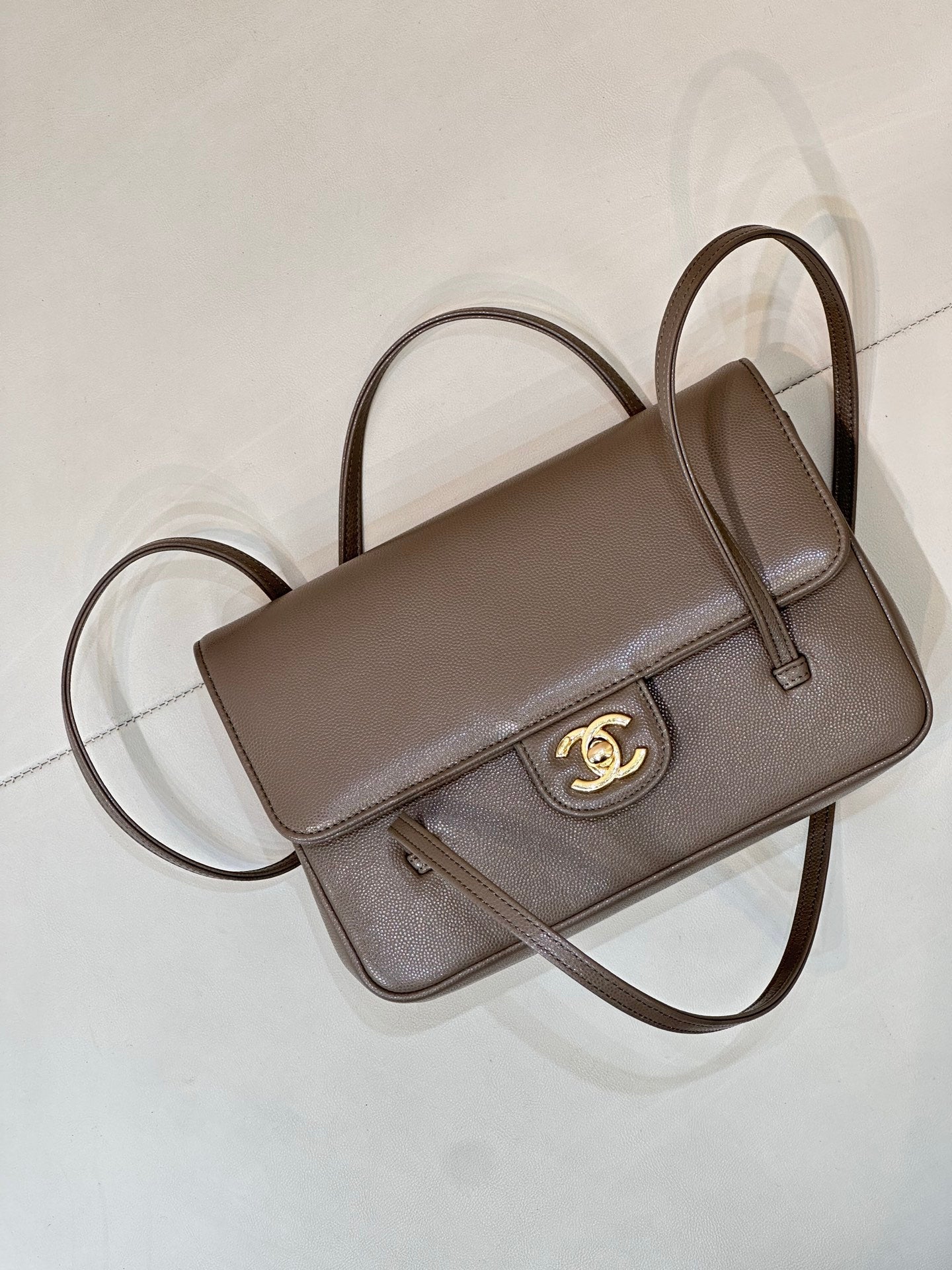 Taupe Chanel shoulder bag angled view with top handle, flap, and gold CC emblem