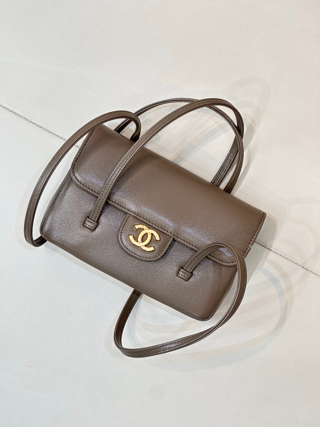 Chanel bag in taupe leather with front flap, gold CC logo, and long shoulder strap.