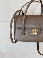 Chanel bag close-up in taupe leather with front flap and gold CC logo clasp.