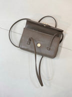 Chanel bag in dark taupe leather with top handles, front flap, and gold button closure.