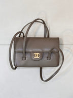 Chanel bag in taupe leather with two top handles, gold CC logo on front flap, and strap.