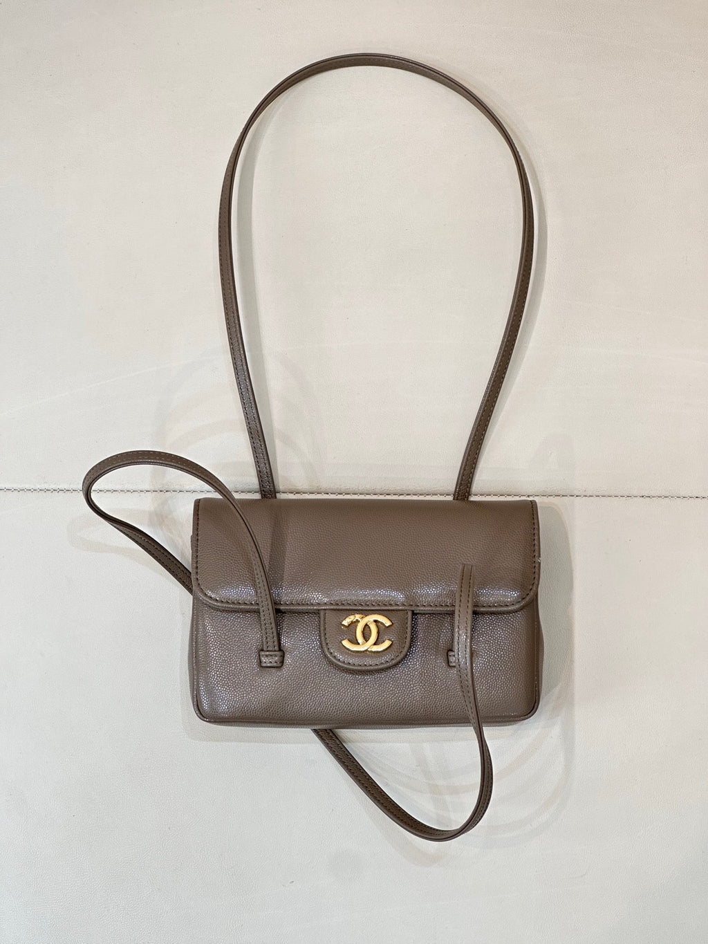 Chanel bag in taupe leather with gold CC logo, front flap, and long crossbody strap.