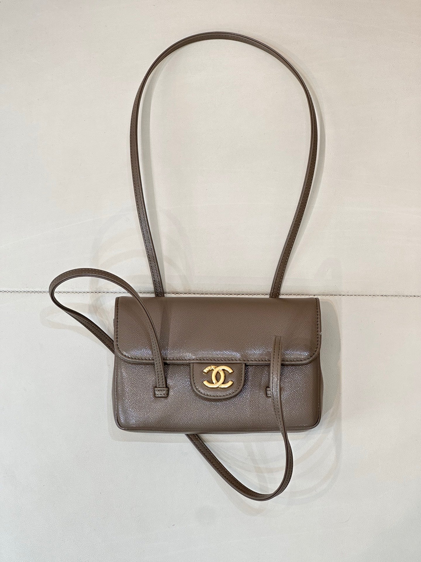 Chanel bag in taupe leather with gold CC logo, front flap, and long crossbody strap.