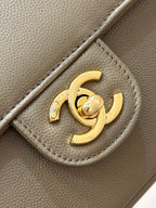 Gold CC logo detail on taupe Chanel bag hardware, with textured leather background.