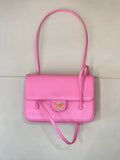 Pink flap handbag with top handle and crossbody strap, gold logo clasp
