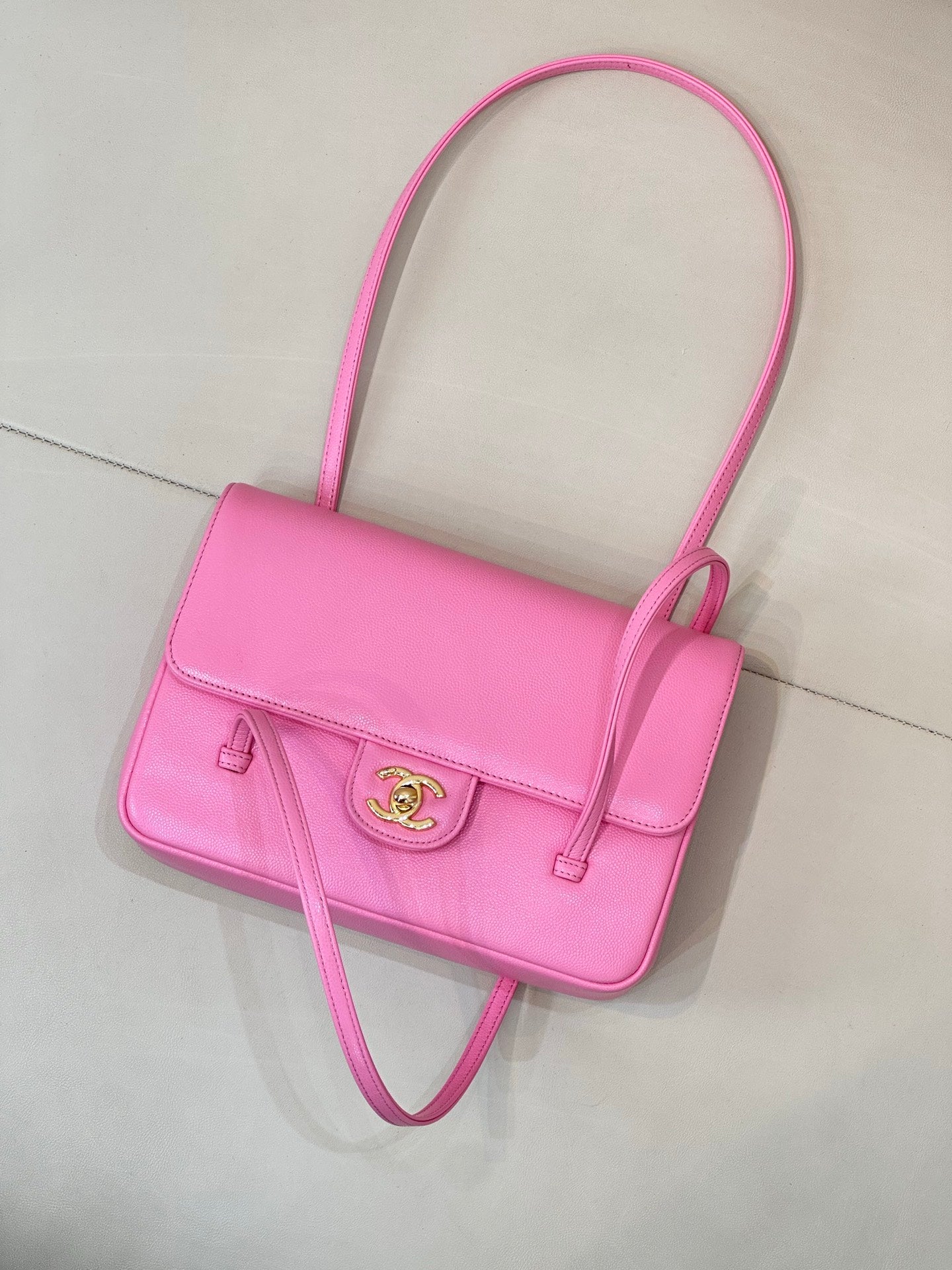 Pink flap handbag with top handle, front logo plate, and crossbody strap
