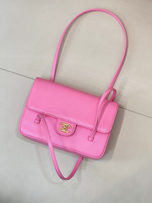 Pink flap handbag with top handle, front logo plate, and crossbody strap