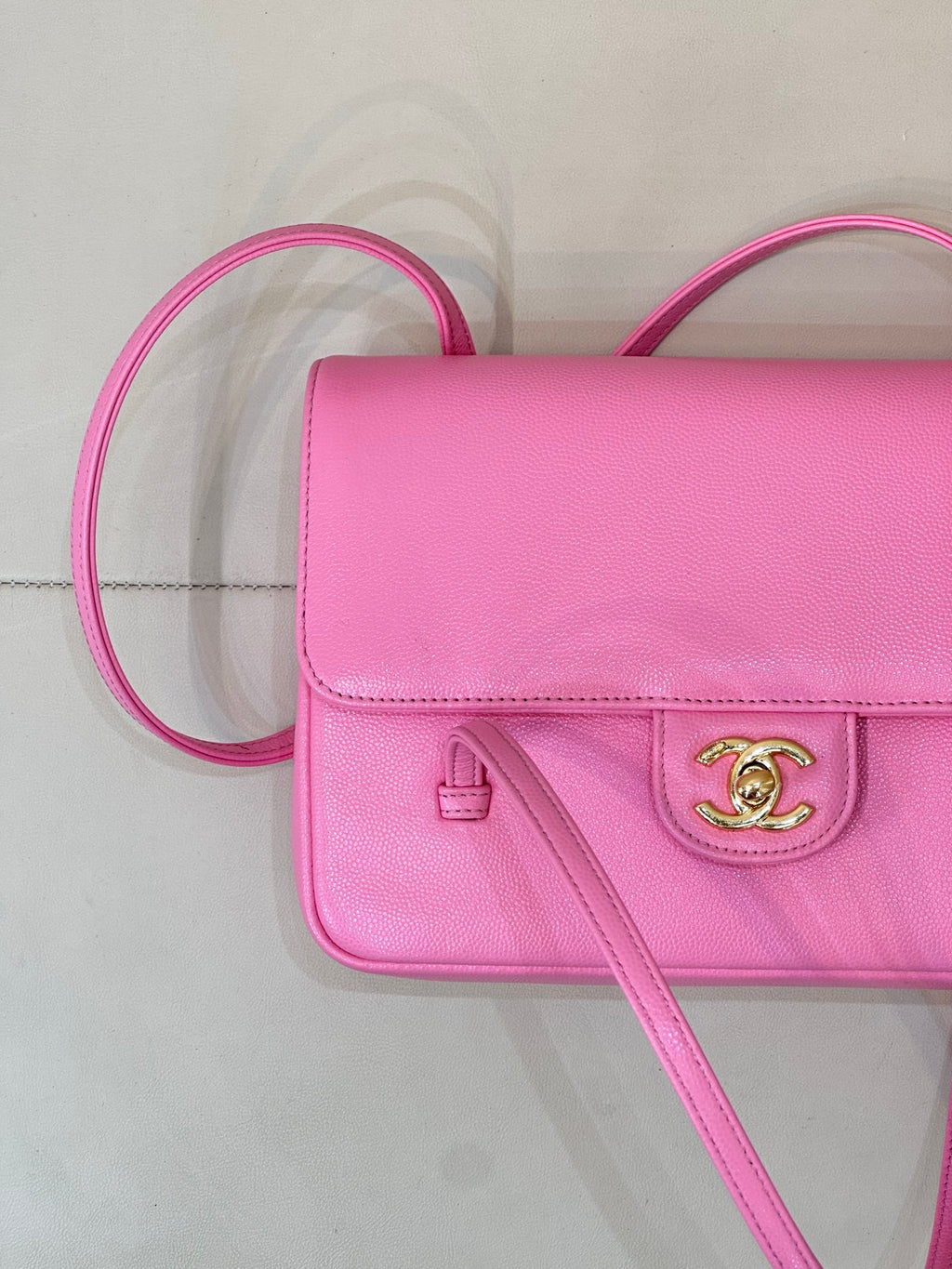 Pink flap handbag detail showing front clasp and logo, with crossbody strap
