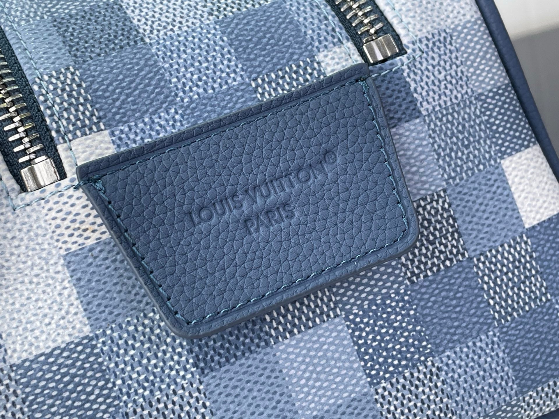 Checkered blue-and-white toiletry bag with textured logo patch on front pocket