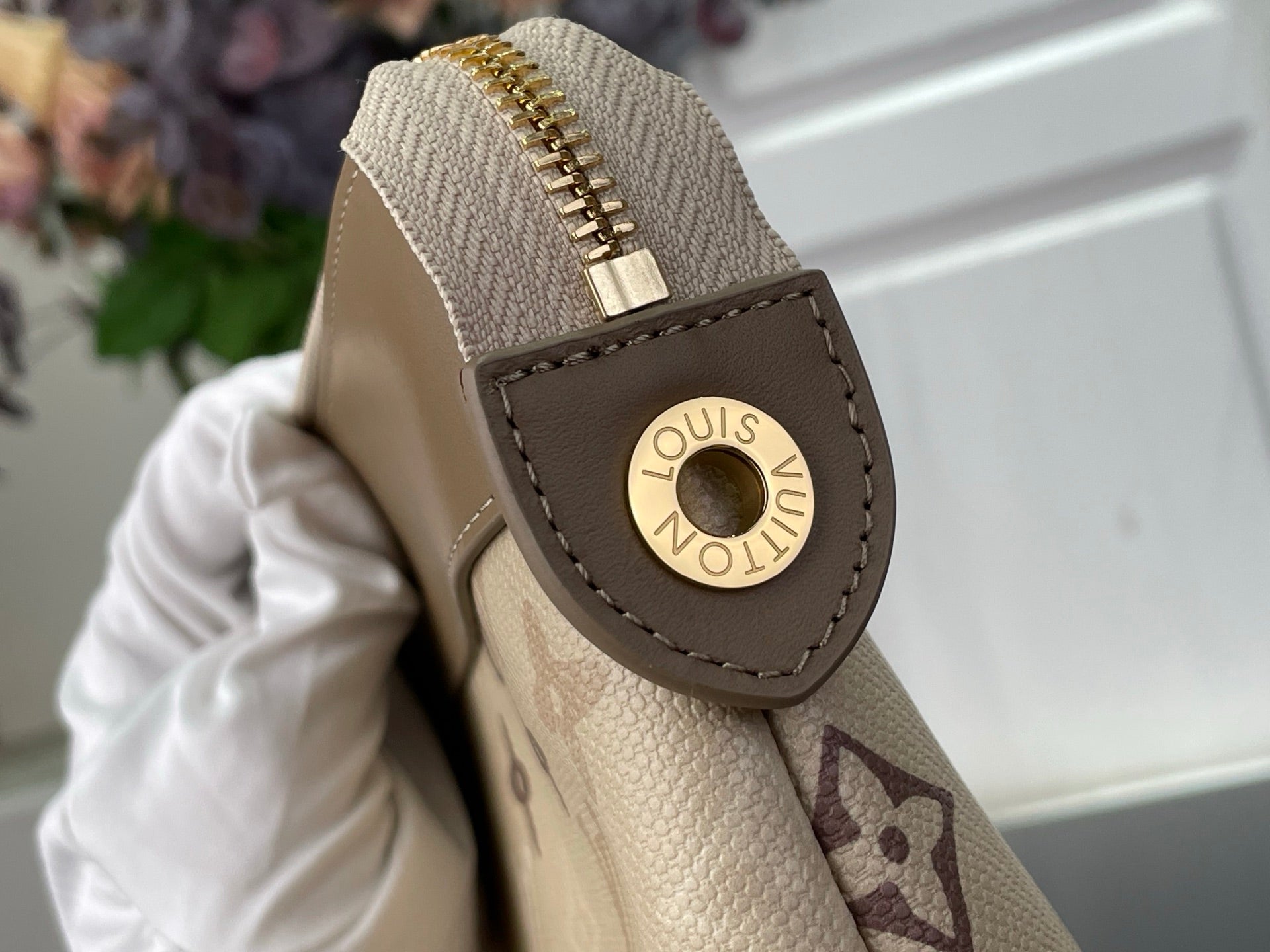 Tan leather loop with gold Louis Vuitton logo on monogram bag corner