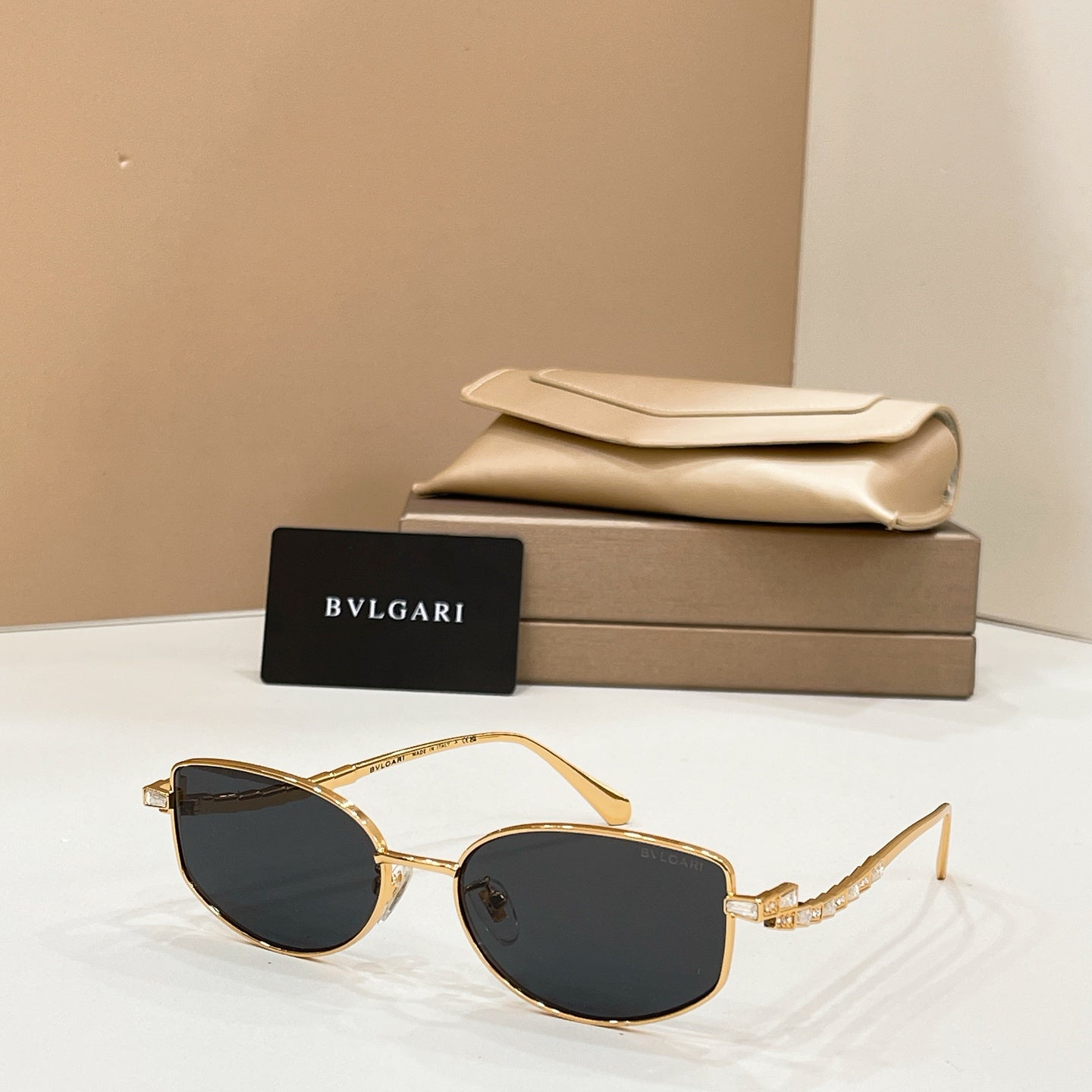 Gold-tone sunglasses with black lenses, shown with beige case