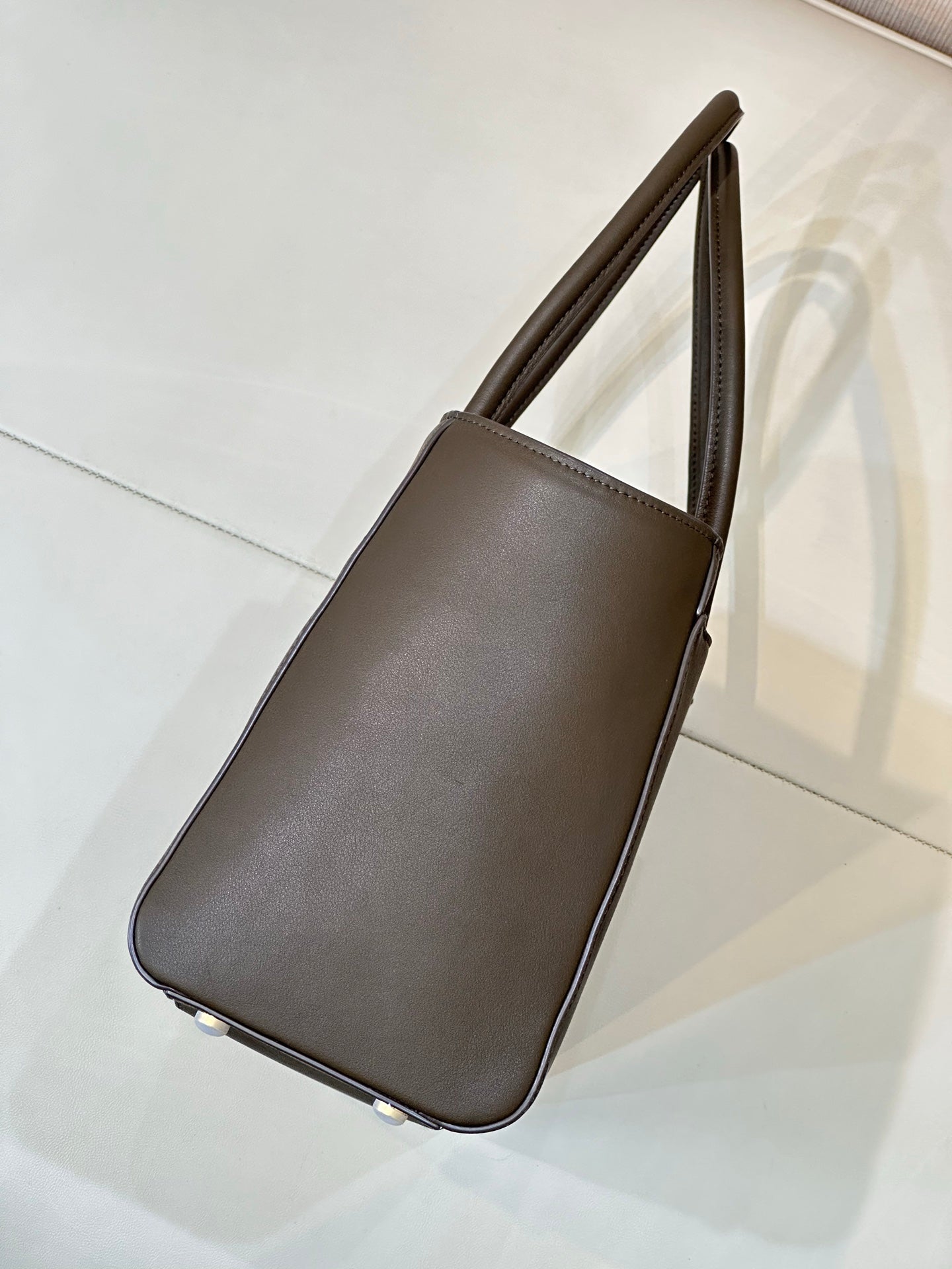 Brown leather tote bag side view with top handles and curved corner edges