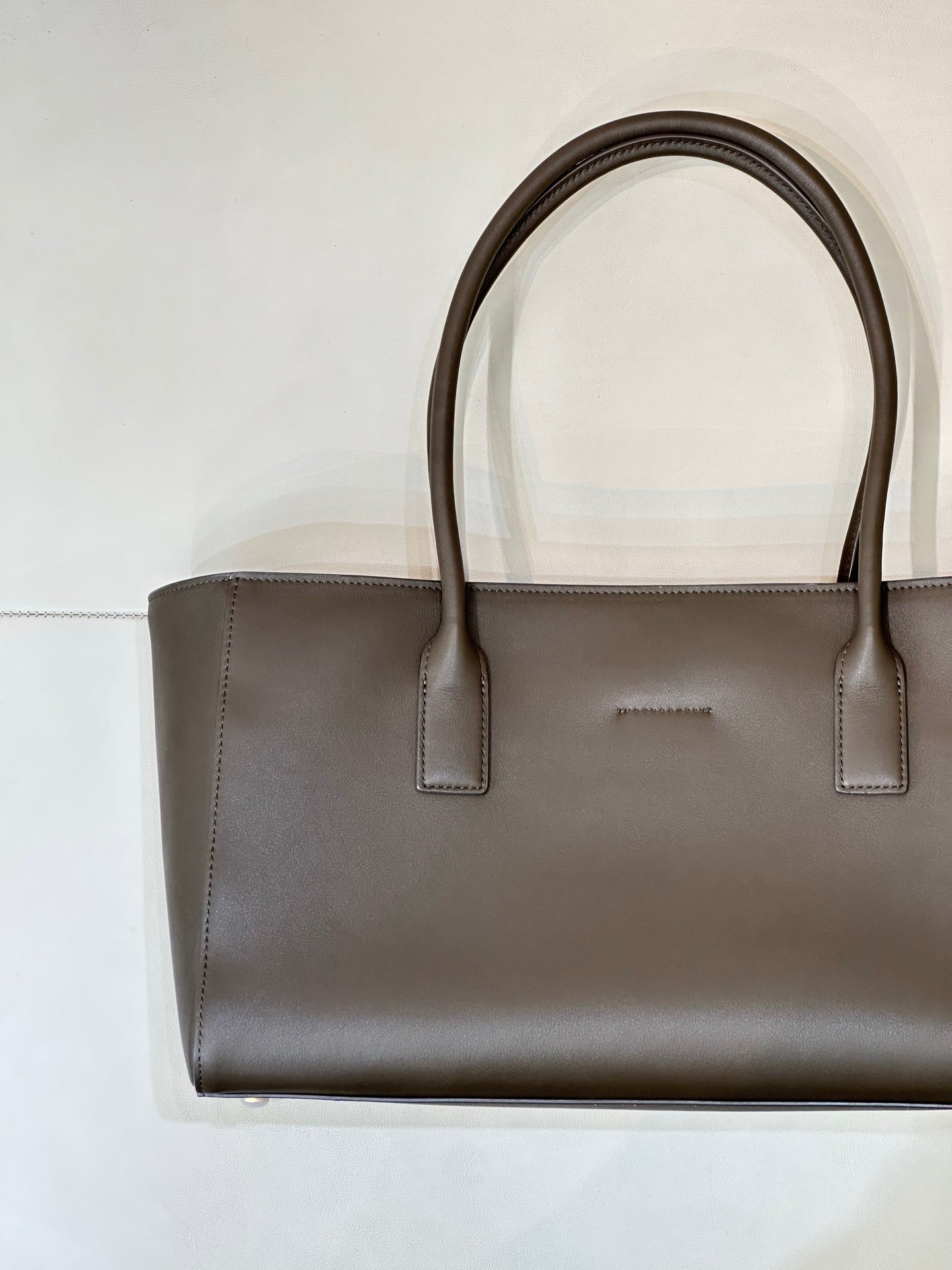 Taupe-brown leather tote bag front view with two top handles and minimal branding