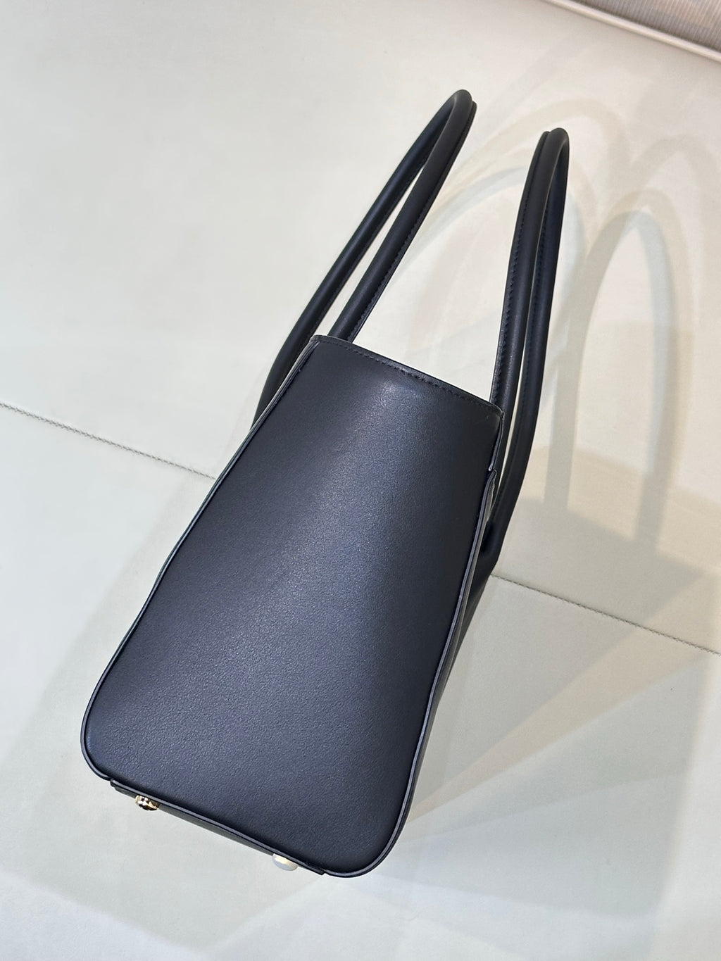 Navy leather tote bag side profile with flat bottom and tall top handles