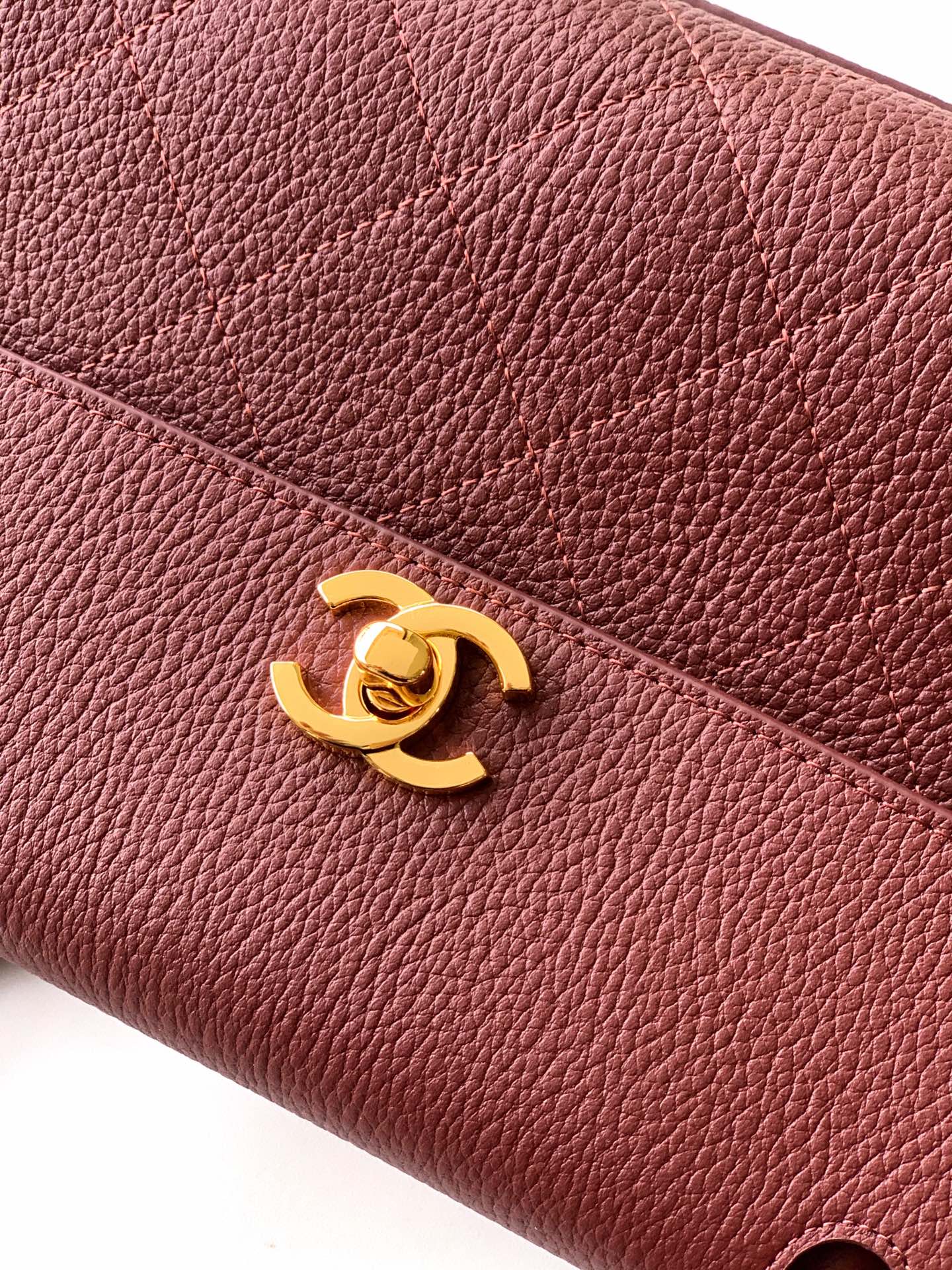 Burgundy Chanel handbag detail with gold CC logo on textured leather